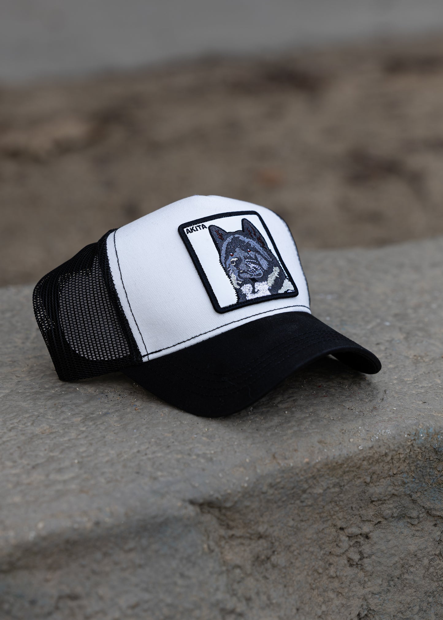 DogKingdom Akita trucker hat – embroidered Akita dog patch cap resting on concrete surface.