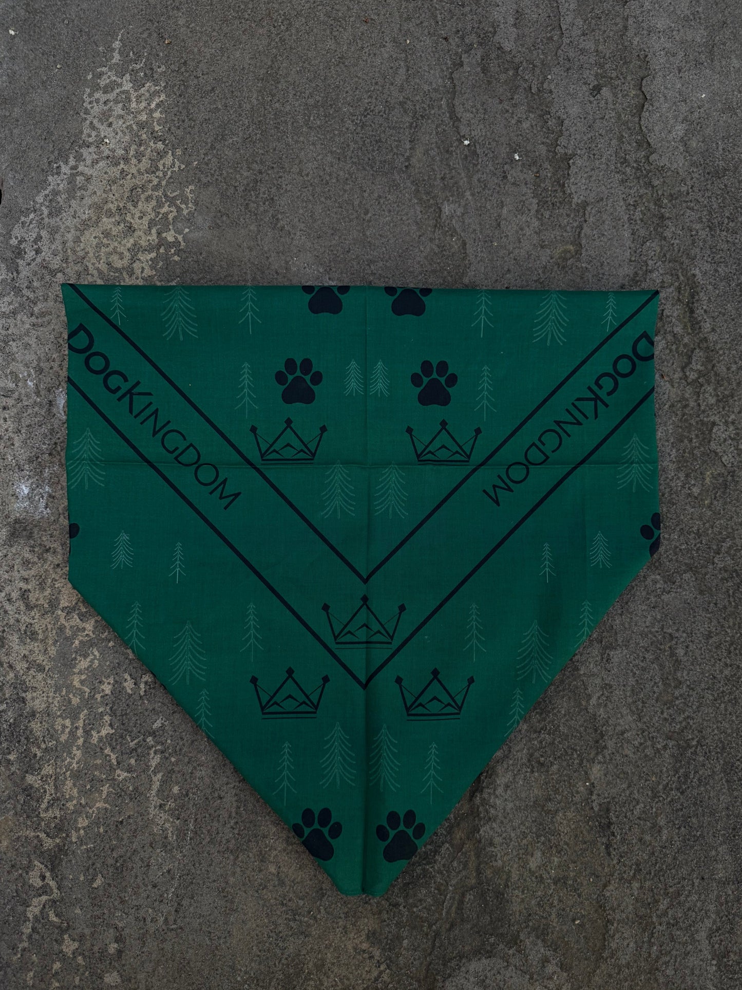 Forest-green DogKingdom cotton bandana with crown, paw print, and tree pattern laid flat on stone